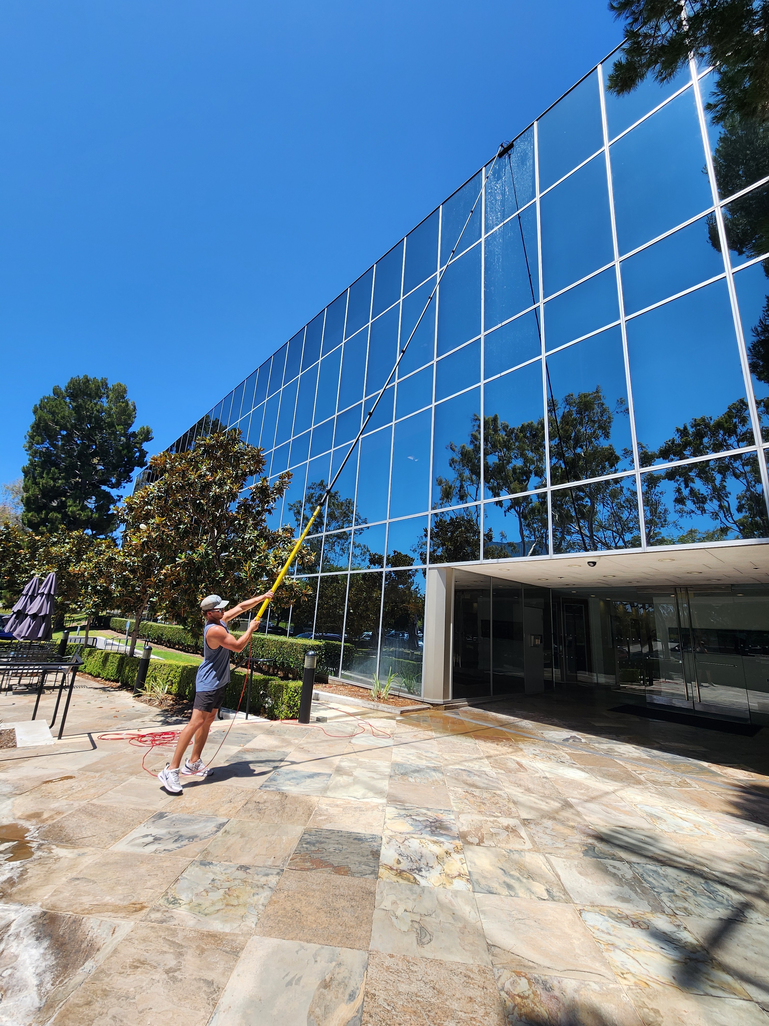 Technician cleaning a glass office building from a stone plaza